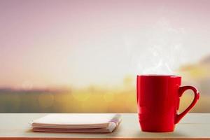 café chaud et cahier sur table et prairies floues au lever du soleil photo