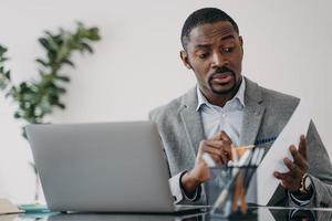 un homme d'affaires afro-américain perplexe discutant d'un projet de travail en ligne par appel vidéo sur un ordinateur portable photo