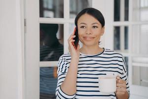 femme heureuse parle sur smartphone. dame debout sur le balcon avec une tasse de café et souriant. photo