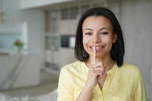 une femme souriante fait un geste de silence à la maison en partageant un secret sur l'offre de la boutique en ligne, les remises, la vente