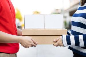 livreur de colis d'un colis par l'intermédiaire d'un service. et gros plan main client femelle acceptant une livraison de boîtes du livreur postal envoie directement à la maison. photo