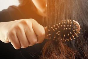 vue arrière jeune femme inquiète du problème de perte de cheveux, du déséquilibre hormonal, du concept de stress. beaucoup de cheveux tombent après avoir peigné la brosse à cheveux à la main. femme démêlé ses cheveux avec un peigne, soins de santé photo