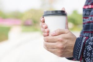 jeune homme main tenant une tasse de papier à emporter en buvant du café chaud sur le café-café. photo