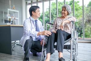 médecin asiatique vérifiant le genou d'un patient âgé en fauteuil roulant, soins de santé et concept médical. photo