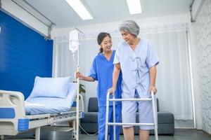 infirmière asiatique aidant un patient âgé essayant de marcher avec une solution saline à l'hôpital, les soins de santé et le concept de médecine. photo