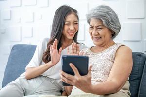 femme asiatique, personne âgée, mère et fille utilisant un smartphone pour un appel vidéo avec bonne humeur souriant et riant sur un canapé à la maison. photo