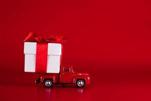 voiture rouge avec une boîte-cadeau sur fond rouge. concept - livraison de cadeaux pour les vacances, la saint-valentin, la journée internationale de la femme, le 14 février, le 8 mars. shopping, vente photo