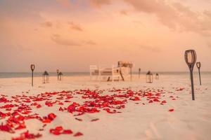incroyable dîner romantique sur la plage avec des bougies et des fleurs sous le ciel coucher de soleil. romance et amour, dîner de destination de luxe, configuration de table exotique avec vue sur la mer. conception d'anniversaire de célébration de lune de miel photo