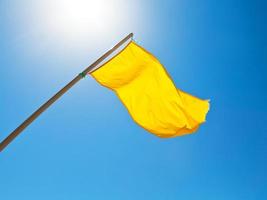 drapeau jaune d'avertissement sous le soleil avec un ciel bleu photo