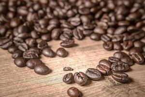 café sur fond en bois. grains de café torréfiés bruns, graines sur fond sombre. espresso noir, arôme, boisson à la caféine noire. gros plan moka énergétique isolé, ingrédient cappuccino. photo
