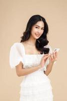jeune femme asiatique à la mode utilisant un smartphone debout sur un fond beige isolé se sentant heureuse. shopping paiement en ligne avec téléphone mobile. femme montrant un téléphone portable à écran vide. photo