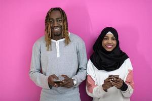 jeune couple afro-américain riant à l'aide d'applications de smartphones isolées sur fond de studio rose photo