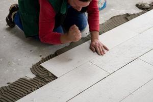 travailleur installant les carreaux en céramique effet bois sur le sol photo