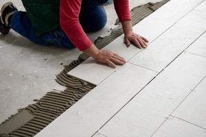 travailleur installant les carreaux en céramique effet bois sur le sol photo