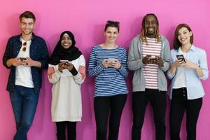 divers adolescents utilisent des appareils mobiles tout en posant pour une photo en studio devant un fond rose