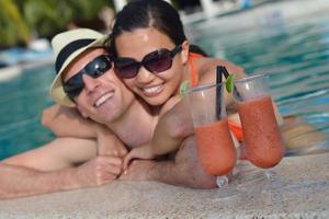 un jeune couple heureux se détend et prend une boisson fraîche au bord de la piscine photo