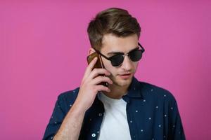 un jeune homme portant une chemise bleue et des lunettes de soleil à l'aide d'un smartphone photo