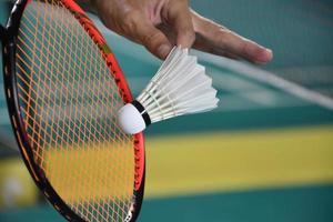 le joueur de badminton tient une raquette et un volant crème blanc devant le filet avant de le servir de l'autre côté du terrain. photo