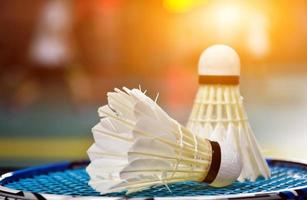 volant et raquette de badminton blanc crème avec ombrage néon sur sol vert dans un terrain de badminton intérieur, arrière-plan flou de badminton, espace de copie. photo