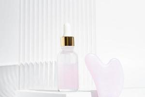 rouleau de massage pour le visage en quartz rose avec bouteille d'huile cosmétique ou de sérum sur fond blanc. le concept de soins de la peau à la maison photo