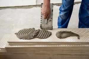 travailleur installant les carreaux en céramique effet bois sur le sol photo