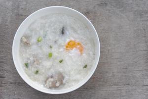 vue de dessus de bouillie de riz ou congee avec œuf dans un bol blanc sur fond de table en bois vintage. photo