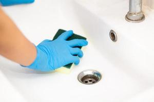 personne, une main dans un gant de caoutchouc bleu sur la photo, enlève et lave le lavabo de la salle de bain photo