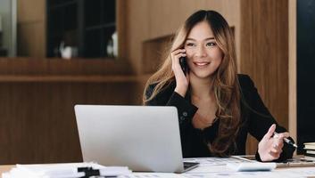 femme d'affaires asiatique a la joie de parler au téléphone, ordinateur portable et tablette sur le bureau. photo