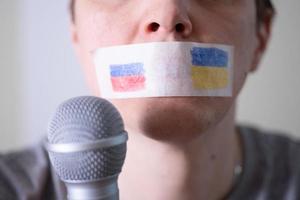 une bouche scotchée avec un drapeau de la russie et de l'ukraine essayant de parler dans un microphone. photo