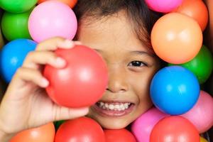 portrait d'une petite fille souriant largement avec des boules en plastique colorées autour d'elle