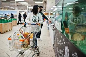 un couple asiatique porte un masque protecteur faisant ses courses ensemble dans un supermarché pendant la pandémie. choisissez des fruits de mer. photo