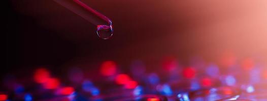 rangée de tubes à essai. concept de laboratoire médical ou scientifique, gouttelette de liquide avec compte-gouttes sur fond bleu rouge, gros plan, photo de micro photographie.