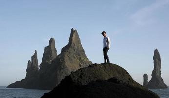 Homme debout sur un rocher à la plage noire de Reynisfjara, Islande, avec le vent dans les cheveux photo