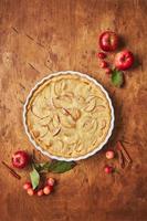 gâteau aux pommes fait maison avec de la crème sure, des pommes rouges, des pommettes et de la cannelle sur fond de bois, vue de dessus photo