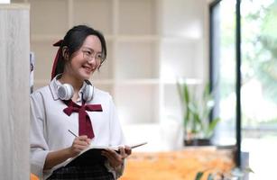 une jeune femme d'affaires asiatique se tient à un bureau et prend des notes dans un cahier. le concept d'éducation et de technologie. photo