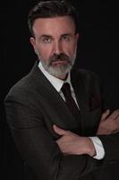 portrait d'un homme d'affaires senior élégant et élégant avec une barbe et des vêtements d'affaires décontractés en studio photo isolé sur fond sombre gesticulant avec les mains