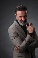 portrait d'un homme d'affaires senior élégant et élégant avec une barbe et des vêtements d'affaires décontractés en studio photo isolé sur fond sombre gesticulant avec les mains