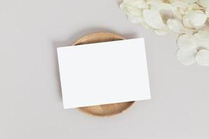 carte de voeux ou carte d'invitation avec des feuilles de fleurs sèches blanches sur une plaque ou un plateau en bois sur fond beige photo