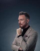 portrait d'un homme d'affaires senior élégant et élégant avec une barbe et des vêtements d'affaires décontractés en studio photo isolé sur fond sombre gesticulant avec les mains