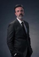 portrait d'un homme d'affaires senior élégant et élégant avec une barbe et des vêtements d'affaires décontractés en studio photo isolé sur fond sombre gesticulant avec les mains