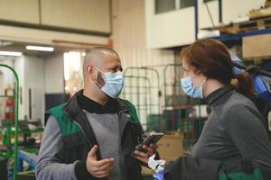 les travailleurs industriels avec des masques faciaux protégés contre le virus corona discutent de la production en usine. personnes travaillant pendant la pandémie de covid-19. photo