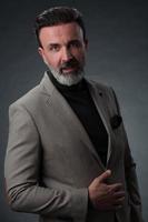 portrait d'un homme d'affaires senior élégant et élégant avec une barbe et des vêtements d'affaires décontractés en studio photo isolé sur fond sombre gesticulant avec les mains