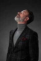 portrait d'un homme d'affaires senior élégant et élégant avec une barbe et des vêtements d'affaires décontractés en studio photo isolé sur fond sombre gesticulant avec les mains