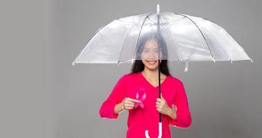 octobre mois de sensibilisation au cancer du sein, femme adulte en robe rose main tenant un ruban rose et un parapluie pour soutenir la protection. espace de copie du concept de la journée internationale des femmes, des mères et du cancer photo