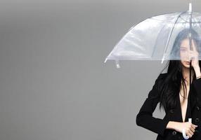 femme transgenre asiatique aux longs cheveux raides noirs, coup de vent en l'air. femme tenir un parapluie contre la tempête de vent, se sentir mode sensuelle sexy, espace de copie isolé sur fond gris photo
