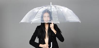 femme transgenre asiatique aux longs cheveux raides noirs, coup de vent en l'air. femme tenir un parapluie contre la tempête de vent, se sentir mode sensuelle sexy, espace de copie isolé sur fond gris photo