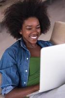 femmes afro-américaines à la maison sur la chaise à l'aide d'un ordinateur portable photo