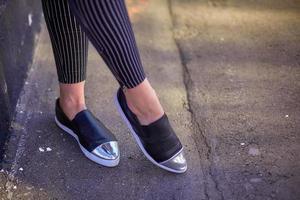 jambes féminines, la fille marche le long de l'asphalte dans des chaussures noires et un jean noir étroit à rayures blanches photo