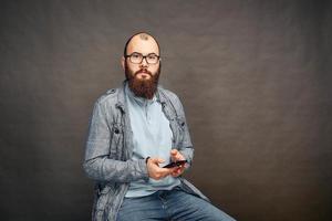 homme barbu à lunettes avec téléphone à la main sur fond marron. photo