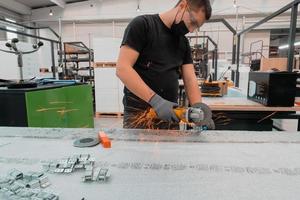 intérieur de l'usine d'ingénierie de l'industrie lourde avec un ouvrier industriel utilisant une meuleuse d'angle et coupant un tube métallique.il porte un masque sur son visage à cause de la pandémie de coronavirus photo